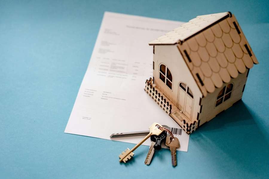 Maquette de maison en bois posée sur un document financier avec des clés illustrant les étapes pour financer un investissement immobilier