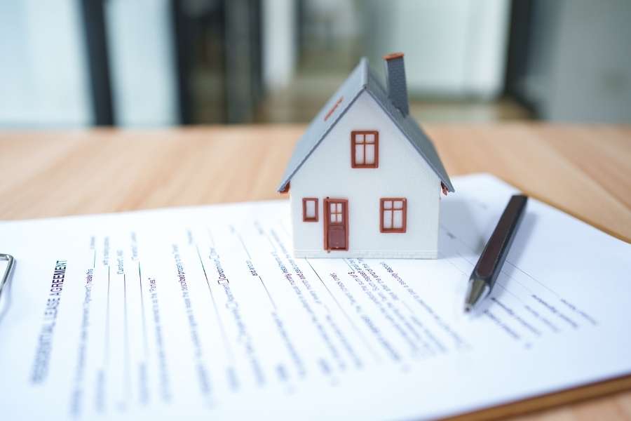 Une petite maquette de maison posée sur un contrat de location de biens pour illustrer un investissement locatif.