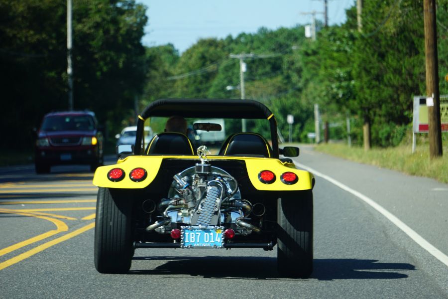 Une voiture décapotable sportive jaune roule sur une route asphaltée, montrant son moteur apparent à l'arrière, illustrant l'impact d'un malus automobile.